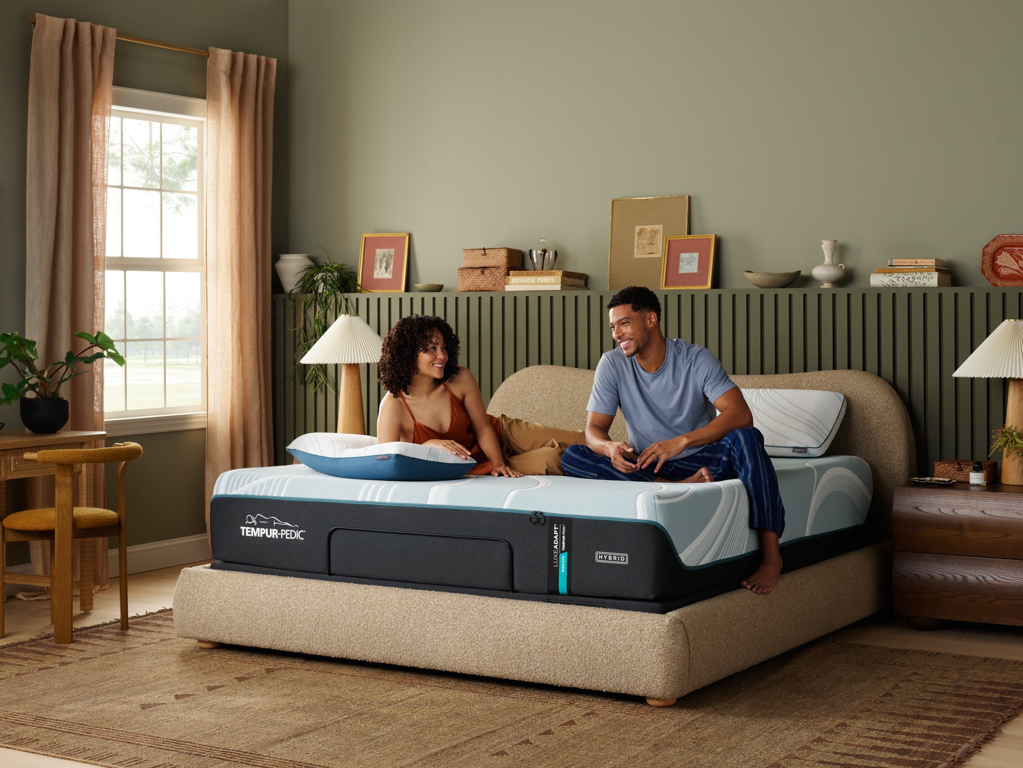 Couple sitting on a Tempur-Pedic mattress in a bedroom setting.