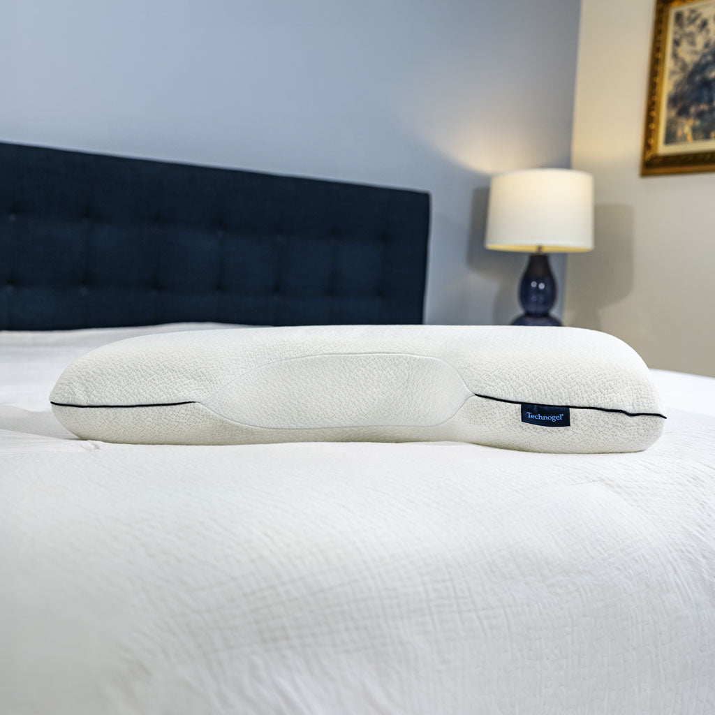 Ergonomic pillow on a bed with a lamp in the background