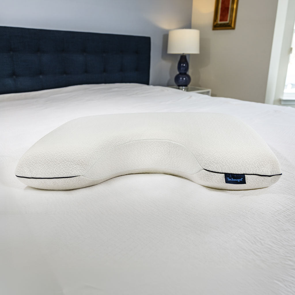 White U-shaped pillow on a bed in a bedroom setting