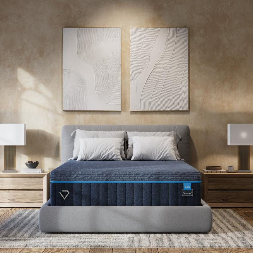 A luxury bed frame with a dark blue quilted mattress and gray headboard and footboard, styled in a warm, modern bedroom with textured beige walls, wooden nightstands, and matching lamps.