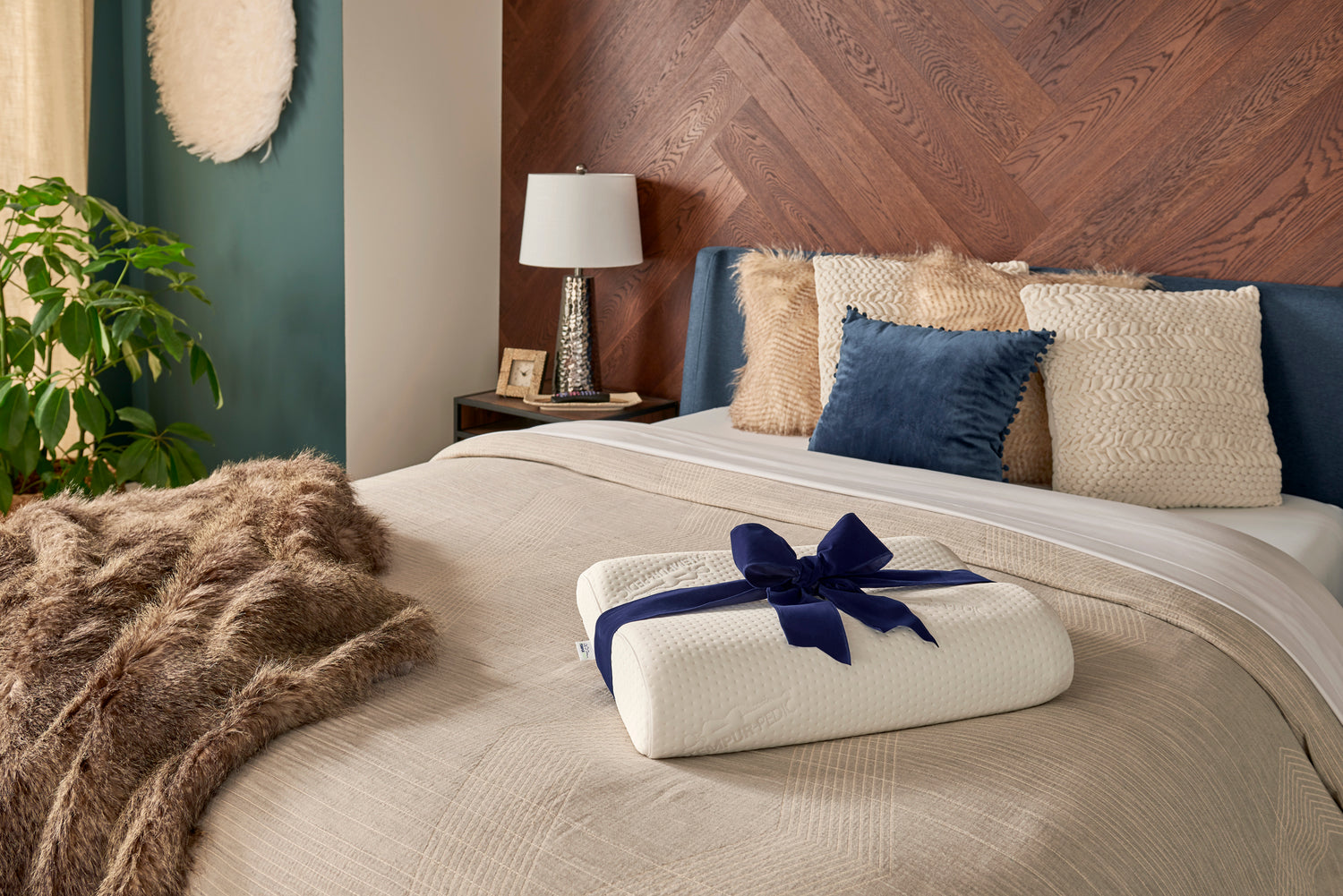 A Tempur-Pedic neck pillow with a navy ribbon on a bed. 