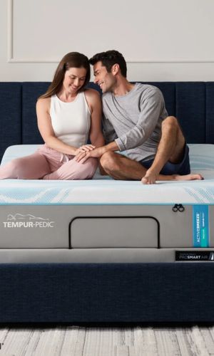 Couple sitting on a Tempur-Pedic mattress, smiling.