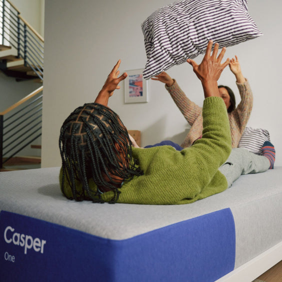Two people playing with pillows on a Casper mattress