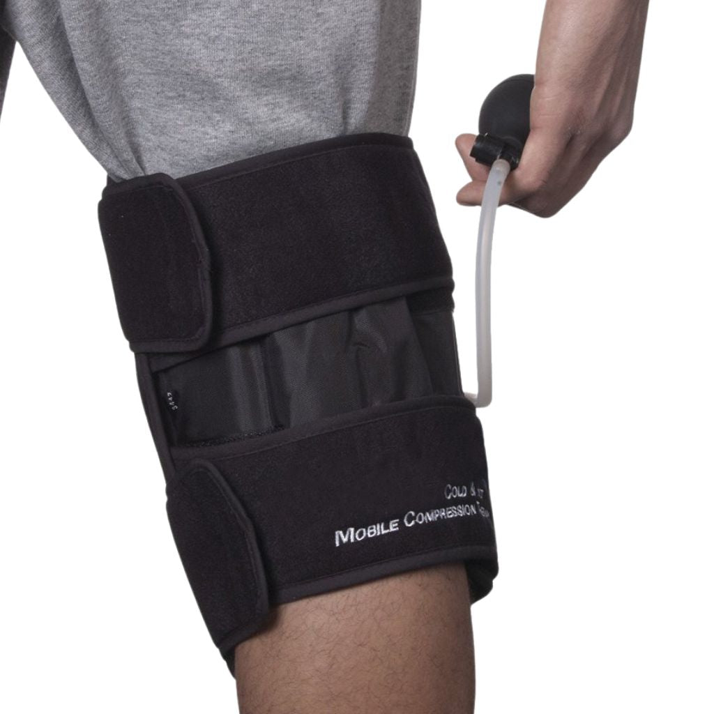 A person wearing a black knee support brace with a hand holding a small black pump connected by a clear tube, against a white background.