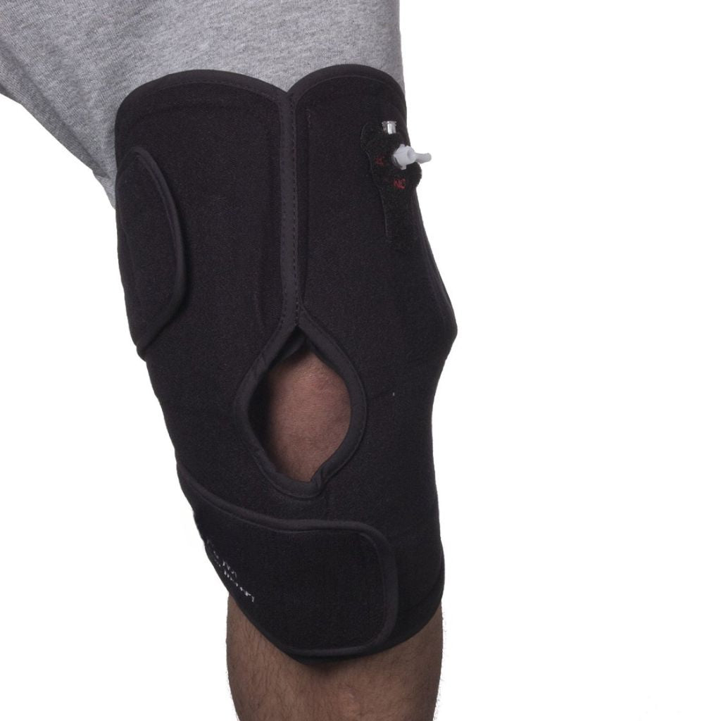 A black knee support brace worn on a person's knee, shown against a plain white background with a gray shirt visible at the top.