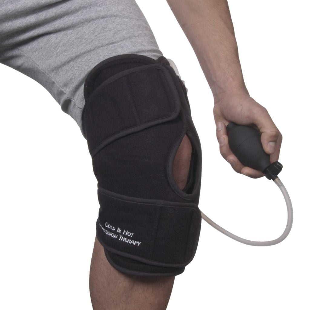 A person wearing a black knee support brace with an attached clear tube and holding a black pump bulb, shown against a white background.
