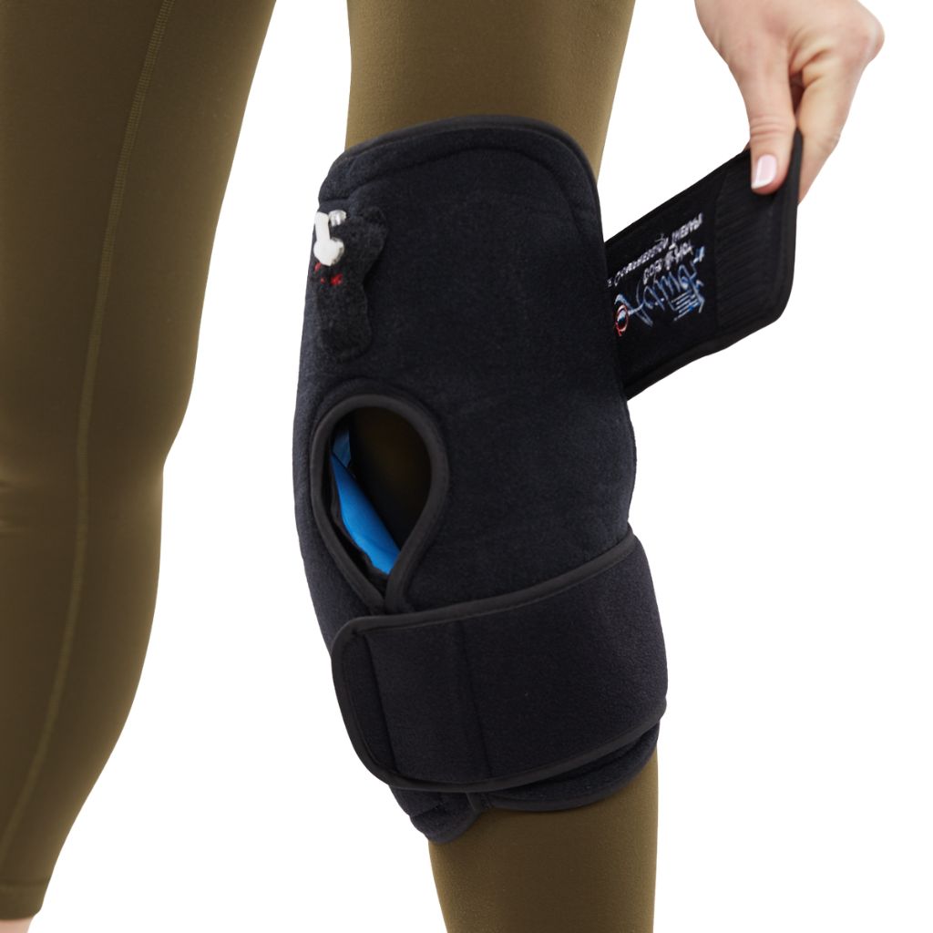 A black knee support brace being fastened onto a person's knee, shown against a plain white background. The brace has a small bear graphic and text on the strap.