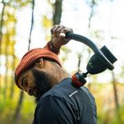 Person holding a massage gun in a forest setting