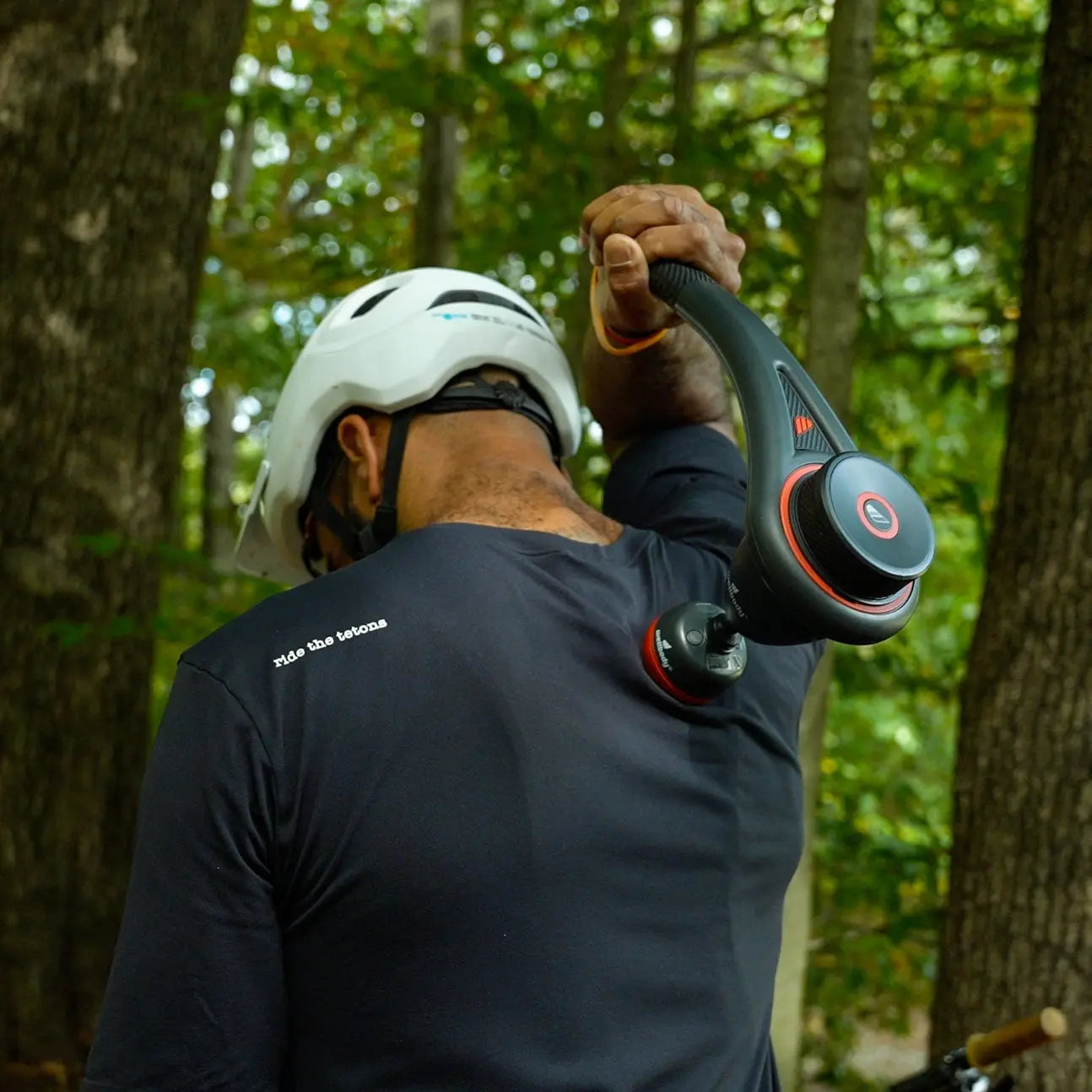 Person wearing a helmet and holding a massage gun in a forest setting