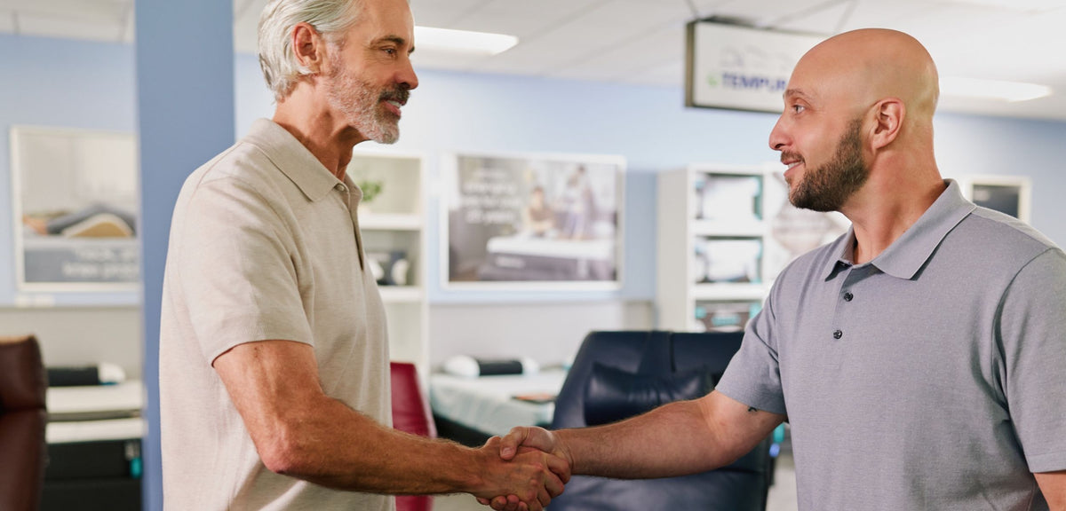 Relax The Back wellness expert welcoming a customer with a handshake inside an ergonomic furniture showroom.