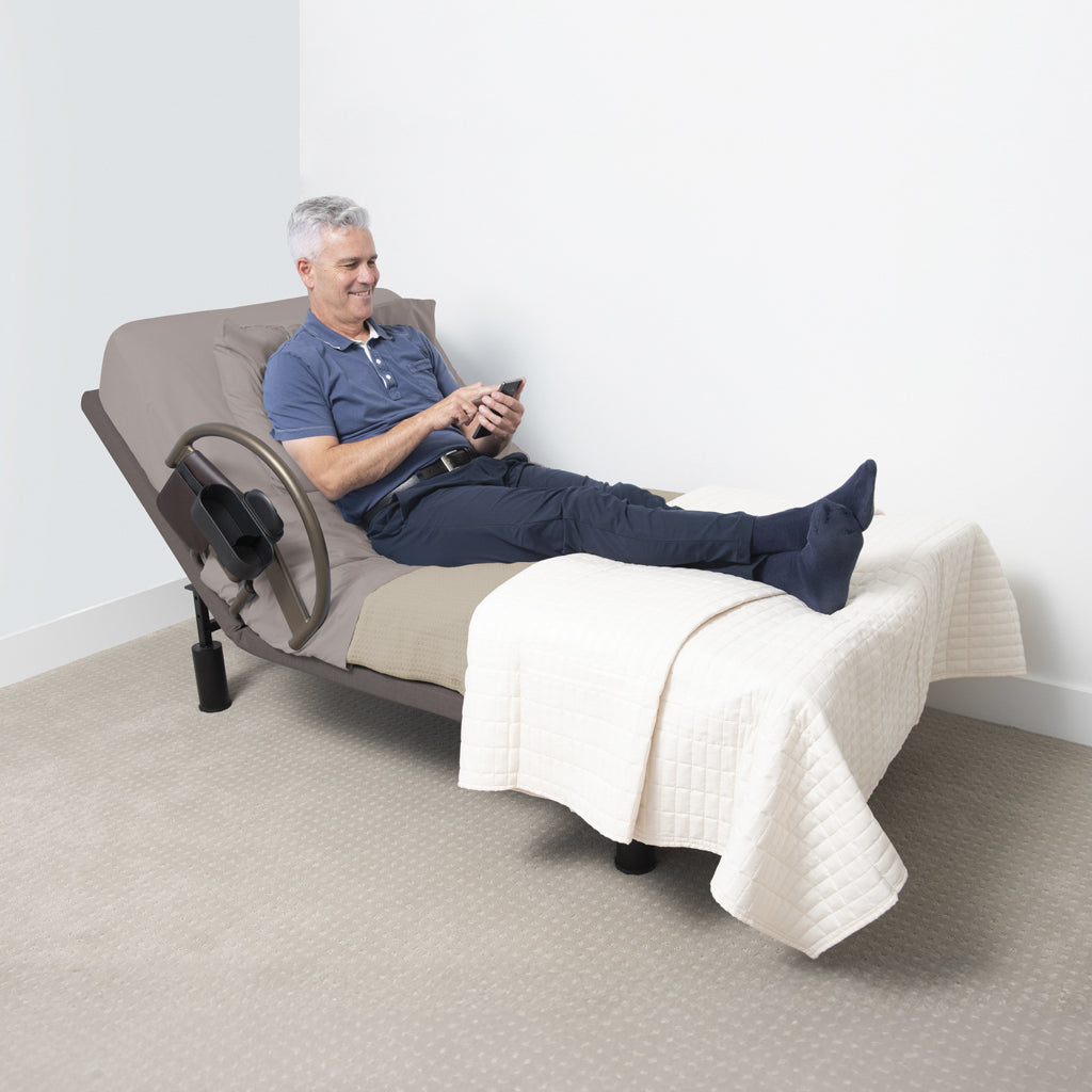 Man using a smartphone while lying on a bed with a bed rail with a blanket on his legs