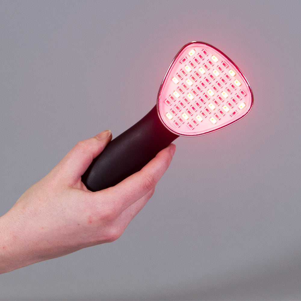 Hand holding a red light device against a gray background