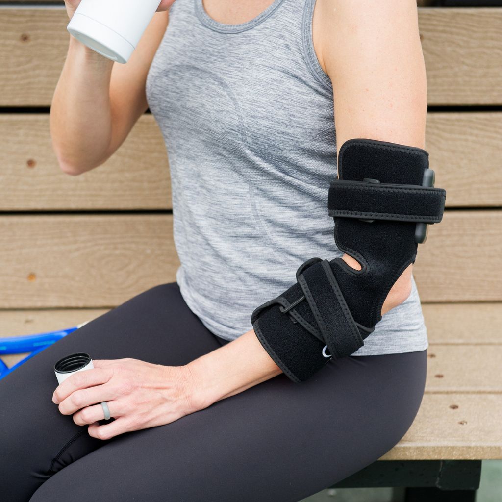 Person sitting on a wooden bench wearing a black arm brace.