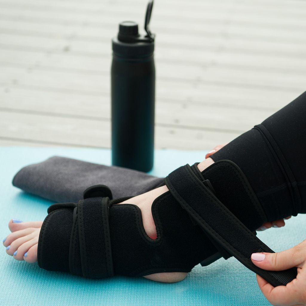 Person wearing a black foot brace on a blue mat with a water bottle in the background
