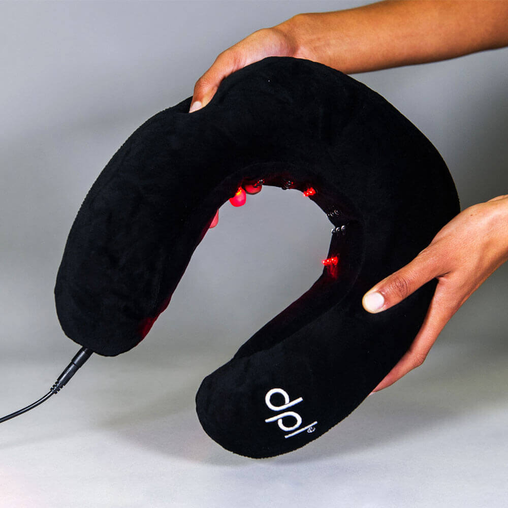 Black neck massager with red lights held by a person against a gray background