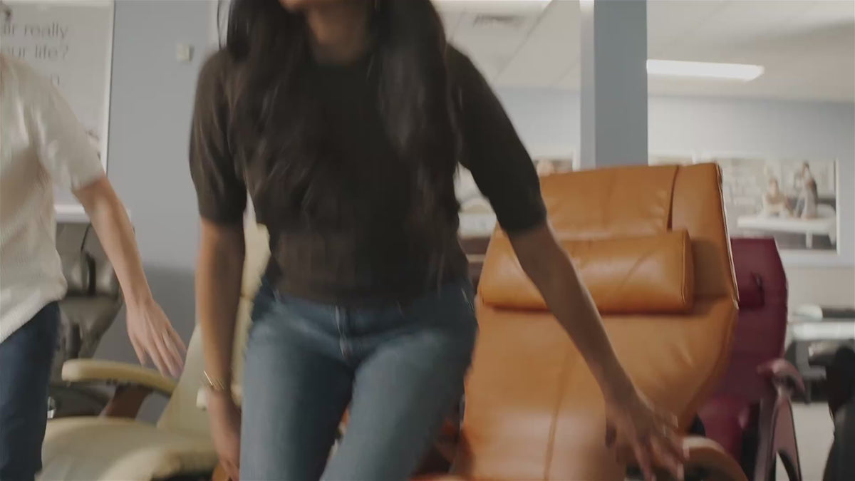 Load video: In a Relax The Back store, a man and woman test zero-gravity recliners, lie back on an adjustable bed with a pillow, and relax in massage chairs. A bald associate in a gray polo guides them through each product, and a gray-haired man dozes in a wood-paneled massage chair at the end.