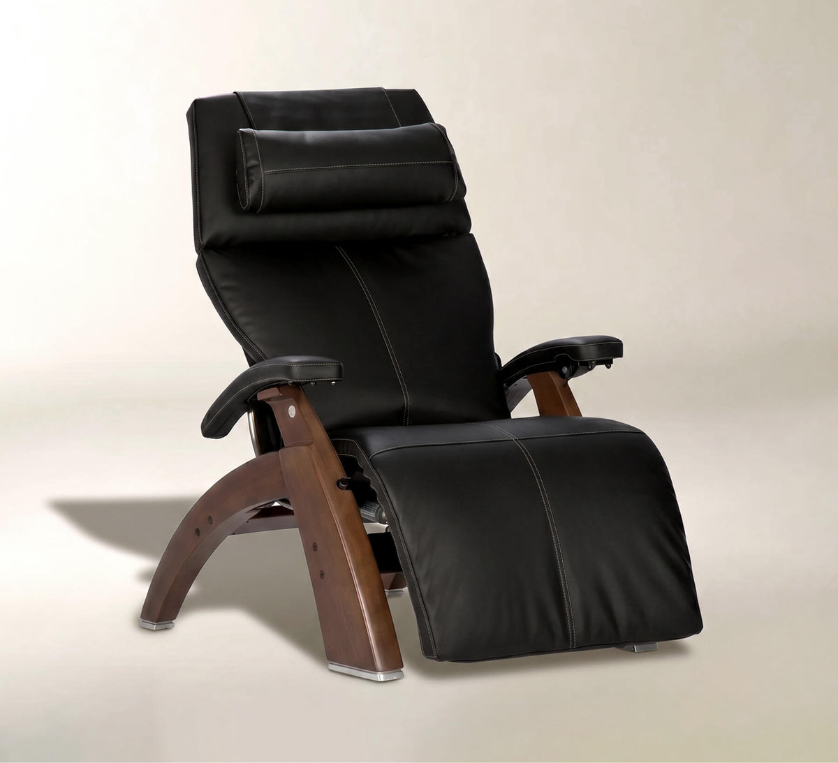 A black leather recliner chair with a headrest pillow, adjustable armrests, and a curved wooden base, shown on a neutral beige studio background.