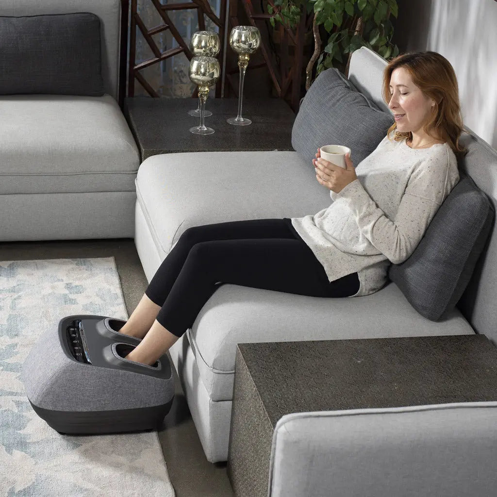 A woman laying on a couch and using the Arch Refresh Foot Massager.
