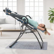 A woman is using the Teeter Fitspine XC5 Inversion Table in a living room setting.