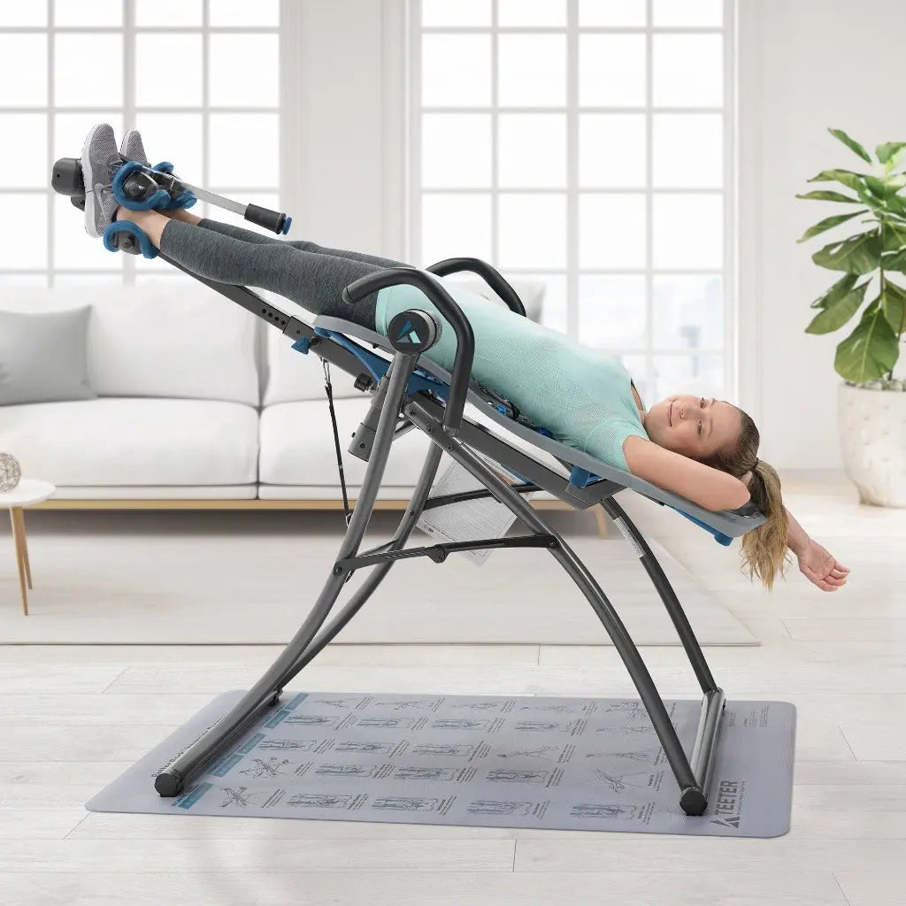 A woman is using the Teeter Fitspine XC5 Inversion Table in a living room setting.