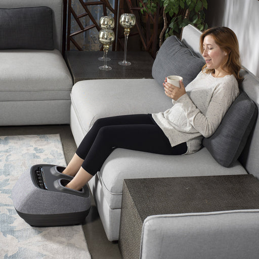 A woman laying on a couch and using the Arch Refresh Foot Massager