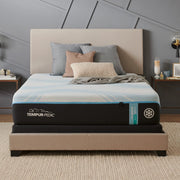 TEMPUR-PRObreeze® 12" Medium Mattress is shown in a bedroom. The bed has a brown fabric, a blanket, and pillows on it