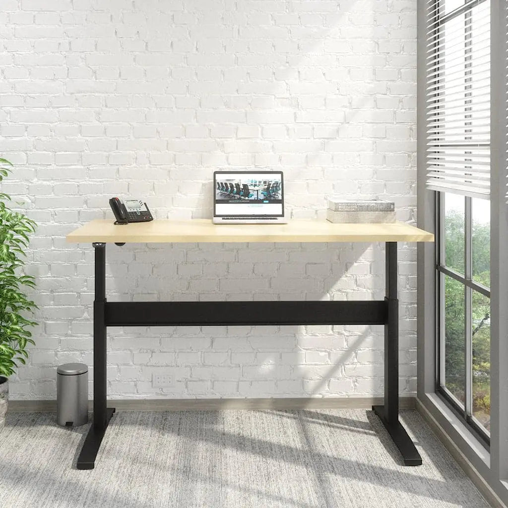 A Transcend Desk positioned beside a window features a laptop and phone on its surface. The desk boasts a wooden top paired with a sleek black base.