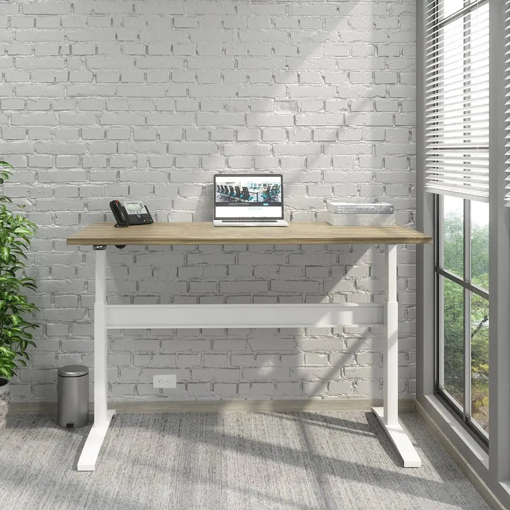 A Transcend Desk positioned beside a window features a laptop and phone on its surface. The desk boasts a stomboli wooden top paired with a sleek white base.